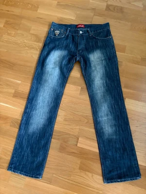 Vintage replay jeans - Säljer ett par blå vintage jeans från Replay med snyggt slitna detaljer. Det är en straight fit modell som lägger sig perfekt över skorna. Jeansen har en broderad Replay-logga på myntfickan och är gjorda i slitstark denim. Perfekta för en avslappnad och trendig look.