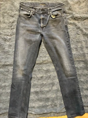 Nudie - Snygga grå slim fit jeans med lätt slitna detaljer och klassisk femficksdesign. Jeansen har en något tvättad look och raka ben. Perfekta för dig som gillar en avslappnad men ändå stilren vibe.
