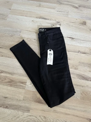 Svarta skinny jeans från ONLY - Säljer ett par svarta skinny jeans från ONLY med hög midja och klassisk femficksdesign. Jeansen har stretchigt material för en bekväm passform och smala ben. Perfekta för dig som gillar en stilren och enkel look.