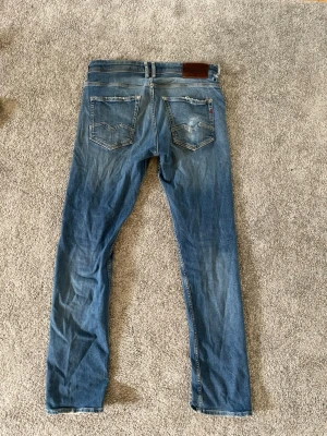 Blå replay jeans  - Säljer ett par blå replay jeans med slitningar och lätt tvättad look. De är i storlek 30 i midjan och 32 längd. Jeansen har fem fickor, dragkedjegylf och klassisk . Perfekta för en avslappnad och trendig stil. Dom har ett litet hål vid midjan men inget stort