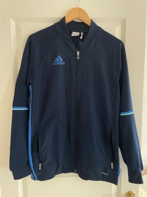 Mörkblå Adidas träningsjacka - Snygg mörkblå träningsjacka från Adidas. Har lite skrynklig märke på utsidan samt lite sönder på insidan 