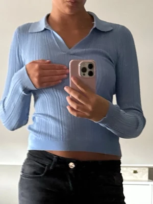 Ljusblå ribbad tröja med krage - Snygg ljusblå ribbad tröja med lång ärm och klassisk krage. Tröjan har en figurnära passform och v-ringad halsringning som ger en trendig look. Perfekt att matcha med jeans eller kjol för en stilren outfit. PRISLAPP KVAR!