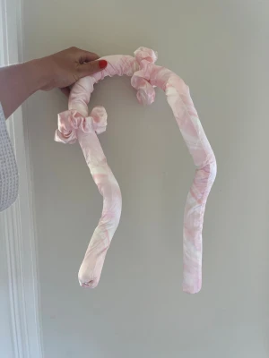 Rosa satin värmespolar för håret - Säljer ett par mjuka värmespolar i ljusrosa satin med rosetter. Perfekta för att skapa lockar utan värme. Materialet är glansigt och lent, och spolarna är flexibla så de är enkla att använda över natten.