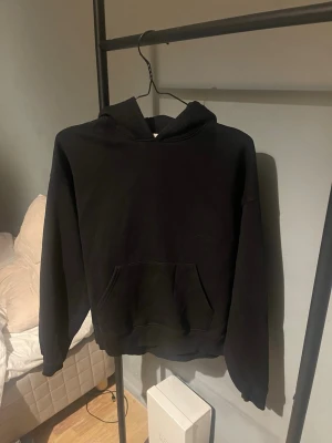 Svart hoodie från Gina tricot - En klassisk svart hoodie från Gina tricot med huva och stor magficka. Tillverkad i mjukt material som känns skönt mot huden. Perfekt för en avslappnad och stilren look. Passar till det mesta och är enkel att matcha med andra plagg.