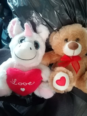 Gosedjur enhörning och nalle - Två mjuka gosedjur, en vit enhörning med rosa horn och ett rött hjärta med texten 'Love', samt en ljusbrun nallebjörn med röd rosett och hjärta på tassen. Perfekta som present eller dekoration.
