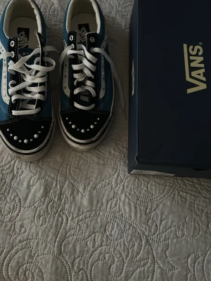 Vans blå och svarta sneakers - Snygga Vans sneakers i blått, svart och vitt med vita snören och dekorativa detaljer på tån. Klassisk låg modell med vit sula och ikonisk sidostrip. Perfekta för dig som vill ha en cool och avslappnad stil.