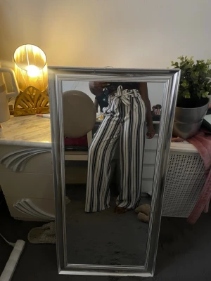 Randiga vida kostymbyxor - Säljer ett par vita kostymbyxor från H&M med svarta vertikala ränder och knytband i midjan. Byxorna har hög midja och vida ben för en avslappnad och trendig look. Perfekta för dig som gillar bekväma men snygga plagg. Haft i flera år men använt endast två-tre gånger. Klippt där nere pga dåvarande längden på byxorna, därav priset. Men inget som påverkar utseendet eller funktionen på byxorna