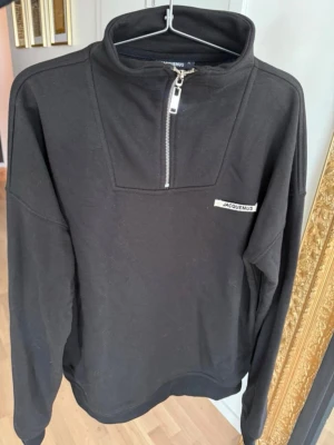 Svart half-zip hoodie  - Svart hoodie  med halv dragkedja framtill och hög krage. Diskret Jacquemus-logga på bröstet. Tillverkad i mjukt material och har en clean, minimalistisk look. Perfekt för dig som gillar stilrena plagg med designer-touch. Fits m/l
