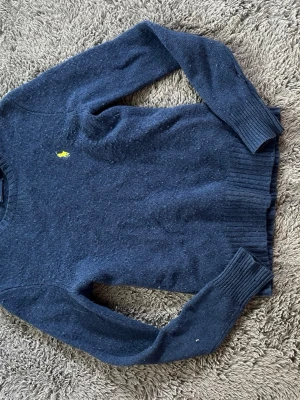 Mörkblå stickad tröja Polo Ralph Lauren - Mörkblå stickad tröja från Polo Ralph Lauren med klassisk gul logga broderad på bröstet. Tröjan har rund halsringning, långa ärmar och ribbstickade muddar vid ärmslut och nederkant. Perfekt för lager på lager och enkel att matcha. I storlek S men känns som xs (enligt mig). Säljer då den aldrig används!☺️