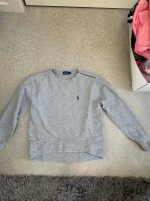 Grå sweatshirt från Polo Ralph Lauren - Stilren och klassisk Polo Ralph Lauren sweatshirt i ljusgråmelerad färg 🤍 Har den ikoniska Ralph Lauren-hästen på bröstet och en snygg dragkedjedetalj vid axeln. Mjuk, bekväm och perfekt för en clean/preppy look ✨ 📏 Strl XS 🤍 Ljusgråmelerad ✨ Fint skick 🐎 Äkta Polo Ralph Lauren Perfekt med jeans, kjol eller mjukisbyxor!                     Nypris ca 2200kr 
