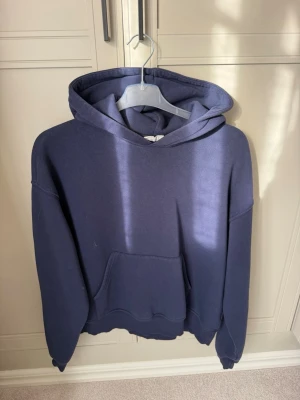 Mörkblå hoodie - Säljer en mörkblå hoodie med huva och stor magficka. Hoodien har en avslappnad look ribbade muddar vid ärmar och nederkant. Perfekt för en chill och casual stil. Materialet känns mjukt och bekvämt, troligen bomull eller bomullsblandning.