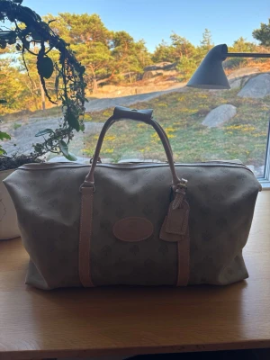 Mulberry beige weekendbag med mönster - Snygg beige weekendbag med diskret mönster och ljusbruna detaljer. Väskan har två handtag, dragkedja och en tag i läderimitation. Perfekt storlek för kortare resor och enkel att bära med sig.
