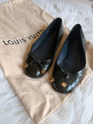 Louis Vuitton ballerinaskor  - Ballerinaskor från Louis Vuitton i grönt. Skorna har en stilren design med en liten rosett framtill, prydd med guldfärgade detaljer med Louis Vuitton-logotypen. Insidan är i läder och sulan är i gummi. Köpta begagnade på Vestiaire.