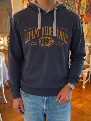 Vintage sällsynt Replay hoodie - Mörkblå hoodie från Replay med gul vintage-tryck på bröstet där det står 'Replay Blue Jeans'. Grå dragsko och insida på huvan. Mjuk bomullsblandning och klassisk passform. Perfekt för en avslappnad och cool stil.