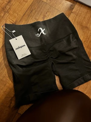 xshapes - Snygga gråa shorts från xshapes med hög midja och scrunch-detalj bak. Stretchigt material som sitter tight och bekvämt. Perfekta för träning eller en sportig look. 