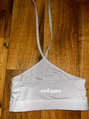 Ljusgrå halterneck-bh xshapes - Snygg ljusgrå bh från xshapes med halterneck och ribbad struktur. Tillverkad i ett stretchigt material som ger en sportig look.