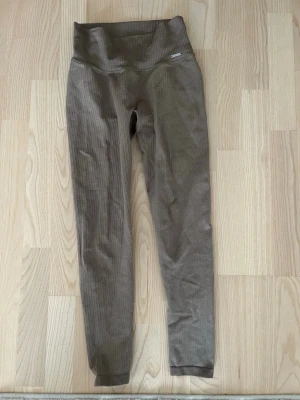 Ribbade bruna tights från Aim'n - Snygga ribbade tights i brun nyans från Aim'n. De har hög midja och är tillverkade i ett stretchigt material som sitter skönt på kroppen. Perfekta för träning eller chill dagar. Metallogo på höften för extra detalj.