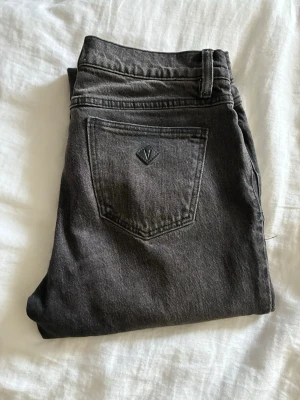 Gråa raka jeans med rå kant - Säljer ett par svarta jeans med rak passform och rå kant nedtill från Abrand modell low straight. Jeansen har klassisk femficksdesign och en diskret logga på bakfickan. Tillverkade i denim med en snygg tvättad look, perfekta till vardagsstilen.