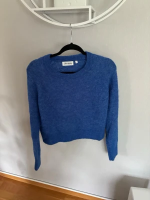 Blå stickad tröja från Carin Wester  - Mysig blå stickad tröja från Carin Wester med rund halsringning, långa ärmar och en kortare modell. Tröjan har en enkel, klassisk design och är tillverkad i ett mjukt material som passar perfekt för kyligare dagar.