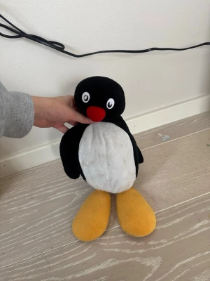Mjuk pingvin gosedjur - Säljer ett gulligt pingvin gosedjur med svart kropp, vit mage, stora gula fötter och röd näbb. Perfekt som present eller mysig inredningsdetalj. Tillverkad i mjukt tyg och har broderade ögon.
