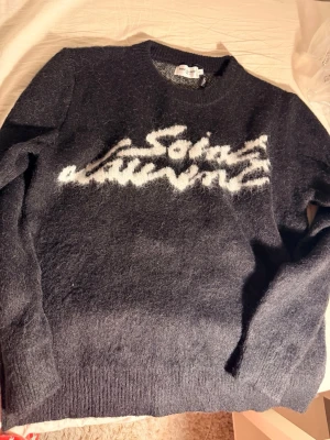 Black sweater YSL - Säljer en svart stickad tröja med vit text i grafisk stil på bröstet. Tröjan är gjord i 100% bomull och har rund hals samt långa ärmar. Perfekt för dig som gillar exklusiva och trendiga plagg.