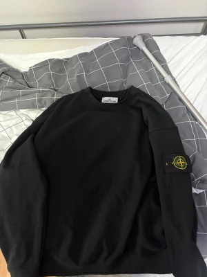 Svart tröja - Säljer en svart tröja från Stone Island med den klassiska loggan på vänster ärm. Tröjan har rund halsringning och är tillverkad i mjukt bomullsmaterial. Perfekt för en clean och stilren look. Helt ny har aldrig använt den.