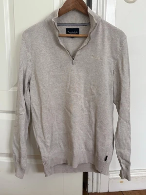 Beige stickad tröja från Bondelid - Snygg beige stickad tröja från Bondelid med halv dragkedja och ståkrage. Tröjan har långa ärmar, ribbade muddar och diskret broderad logga på bröstet. Perfekt för en stilren och avslappnad look.
