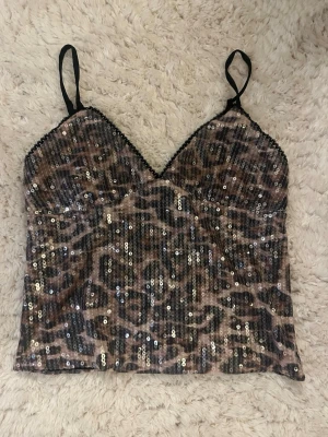 Leopardmönstrad paljettopp - Snygg leopardmönstrad topp med tunna axelband och paljetter. Har bara använt typ två gånger. Storleken är M men jag skulle säga att den är rätt så liten i storleken och passar mig som brukar ha S!