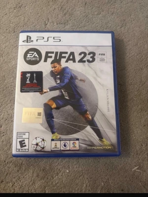 FIFA 23 till PS5 - FIFA 23 till PlayStation 5 är ett fotbollsspel från EA Sports med Kylian Mbappé på omslaget. Spelet har en blå plastbox och erbjuder HyperMotion-teknologi för realistisk spelupplevelse. Perfekt för dig som älskar fotboll och gaming.