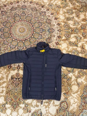 Mörkblå dunjacka från Parajumpers - Snygg mörkblå dunjacka från Parajumpers med gul detalj vid kragen och patch på ärmen. Jackan har dragkedja framtill, två sidofickor med dragkedja och quiltad design. Perfekt för kalla vinterdagar och riktigt stilren look. Priset kan sänkas vid snabba äffärer 