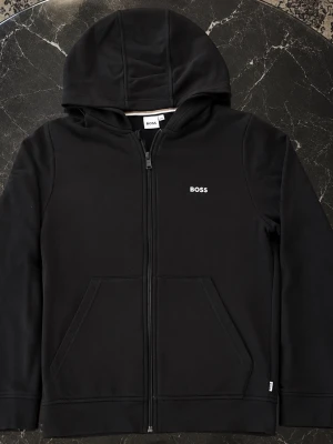 BOSS svart hoodie 14S – mycket fint skick - Snygg och stilren svart hoodie från BOSS, storlek 14S. Har hel dragkedja, huva, känguruficka och diskret BOSS-logga på bröstet. Dragkedjans dragare är även märkt med BOSS, vilket ger en snygg detalj. Hoodien är i väldigt bra skick och väl omhändertagen. Inga hål, fläckar eller andra tydliga skador. Märke: BOSS Storlek: 14S Färg: Svart Skick: Väldigt bra skick