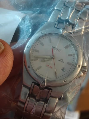 Tissot PR 200 silverfärgad klocka - Klassisk Tissot PR 200 armbandsklocka i silverfärgat stål med vit urtavla och datumvisning. Klockan har tydliga index, röd sekundvisare och är vattentät upp till 200 meter. Länkat armband i metall ger en stilren look.