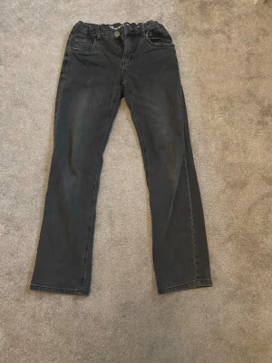 Svarta raka jeans med resårmidja - Säljer ett par svarta jeans med raka ben och resår i midjan. Jeansen har klassiska fem fickor och knappgylf. Materialet ser ut att vara bomullsdenim med lite stretch. Perfekta för en avslappnad och stilren look.