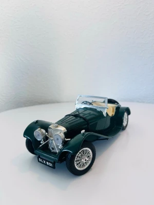 Mörkgrön modellbil klassisk cabriolet 1:18 - Säljer en detaljerad modellbil i metall och plast, föreställande en klassisk mörkgrön cabriolet med beige inredning. Bilen har kromade detaljer, öppet tak och vita ekerfälgar. Perfekt för dig som gillar samlarbilar eller vill ha en snygg inredningsdetalj.