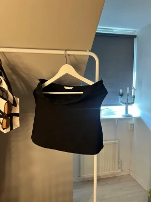 Svart axelbandslös topp - Snygg svart axelbandslös topp med bred krage och rak passform. Perfekt för att skapa en stilren och trendig look. Toppen har en minimalistisk design och är lätt att matcha med olika outfits.bandou top
