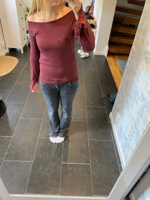 Vinröd off shoulder topp - Trendig vinröd off shoulder topp med långa ärmar och smal passform. Toppen har en snygg asymmetrisk halsringning och är tillverkad i ett mjukt, stretchigt material som sitter bekvämt mot kroppen.