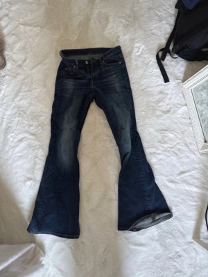 Mörkblå bootcut jeans - Säljer ett par mörkblå low waist bootcut jeans med snygg slitning! 