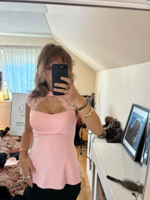 Ljusrosa topp med spetsdetaljer - Supersöt ljusrosa topp med spets vid axlarna och en unik halsringning. Toppen har figurnära passform och är ärmlös, perfekt för dig som vill ha en feminin och trendig look. Materialet känns mjukt och följsamt.
