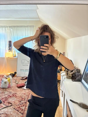 Svart loose topp med kort ärm - En svart loose topp med kort ärm och rund hals. Toppen har en enkel design med små dekorativa hål på ärmen. Perfekt till jeans eller kjol för en avslappnad look.