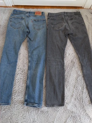 Levi's 502 blå jeans & Lee rider jeans gråa - Säljer ett par klassiska blå Levi's 502 jeans och ett par gråa Lee rider jeans med raka ben och klassisk passform. Jeansen har den ikoniska läderlappen bak i midjan och röd Levi's-tag på bakfickan. Perfekta för en avslappnad och tidlös stil. (Blå Levis jeans storlek 29/32) (gråa Lee jeans storlek 30/32) 300kr st eller 500kr för båda 