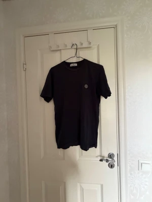 Svart t-shirt med liten logga - En enkel svart t-shirt med rund hals och korta ärmar. På bröstet finns en liten rund logga som ger en clean och stilren look. Perfekt till jeans eller shorts för en avslappnad stil. Pris kan diskuteras 