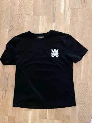 Svart t-shirt från Amiri med tryck - Snygg svart t-shirt från Amiri med vit logga på bröstet och stort AMIRI-tryck på ryggen. Klassisk rund hals och korta ärmar. Perfekt för dig som gillar streetwear och vill ha något stilrent men ändå med attityd.