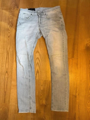 Dondup jeans - Säljer ett par ljusblå slim fit jeans med klassisk femficksdesign och dragkedjegylf. Jeansen har en snygg tvättad look och raka ben. Perfekta för en avslappnad och trendig stil.
