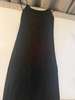 Svart smockad klänning med tunna band - Trendig svart klänning med smockat tyg och tunna axelband. Klänningen har en rak passform och stretchigt material som ger en bekväm känsla. Perfekt för dig som gillar minimalistisk stil och vill ha något enkelt men snyggt.