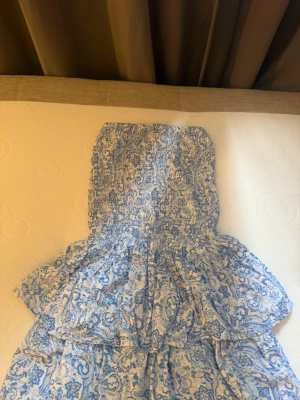 Blåvit kortklänning  XS - Supersöt blåvit kortklänning  i storlek XS. Klänningen har smock upptill och volangdetaljer, samt ett vackert blommigt mönster. Perfekt för varma dagar och ger en fräsch och somrig look.