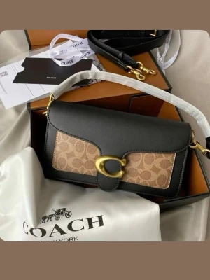 Coach svart och beige handväska - Snygg axelremsväska från Coach i svart läder med beige canvasdetaljer och klassiskt Coach-mönster. Väskan har guldfärgade metalldetaljer och ett stort C-spänne framtill. Justerbar axelrem och kompakt, boxig form som ger en trendig look.