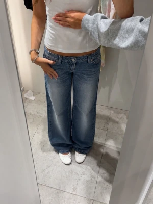 Blåa vida jeans med låg midja - Säljer ett par blåa jeans med låg midja och breda, raka ben. Jeansen har klassisk femficksdesign och ljus tvätt med. Perfekta för en avslappnad och trendig look. 26/32!!🥰