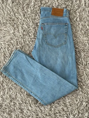 Ljusblå jeans från Levi's 502 - Säljer ett par klassiska 502 ljusblå jeans från Levi's med rak passform och femficksdesign. Jeansen har normal midja och är tillverkade i slitstark denim. Perfekta för dig som gillar en tidlös och avslappnad stil.