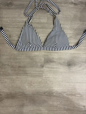 Randig trekantsbikini topp - Säljer en snygg trekantsbikini med marinblå och vita ränder. Klassisk modell med knyt i nacken och ryggen. Perfekt för lata dagar på stranden eller poolen. Materialet känns mjukt och följsamt mot huden.