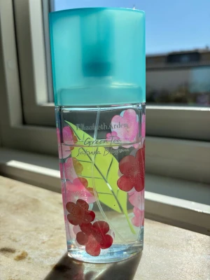 Elizabeth Arden Green Tea Sakura Blossom - Fräsch parfym från Elizabeth Arden i serien Green Tea Sakura Blossom. Flaskan är transparent med rosa blommor och gröna blad som dekoration, och har ett turkost lock. Doften är inspirerad av grönt te och körsbärsblom, perfekt för dig som gillar lätta och blommiga toner. Flaskan rymmer 100ml ,det finns 60 ml kvar .